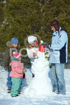 Portrait of family of four making snowman in park Stock Photos