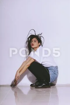 Portrait of fashion model crouching on tiled floor against white wall Stock Photos