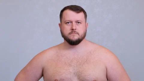Portrait of a fat bearded man naked on a torso on a gray background. Stock Photos