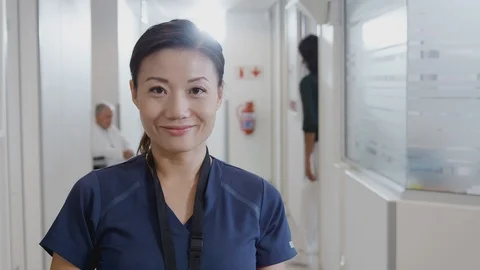 Portrait Of Female Nurse Wearing Scrubs With Digital Tablet In Busy Hospital Stock Footage