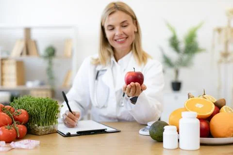 Portrait of female posing with apple while doing paperwork in doctor's office. Stock Photos
