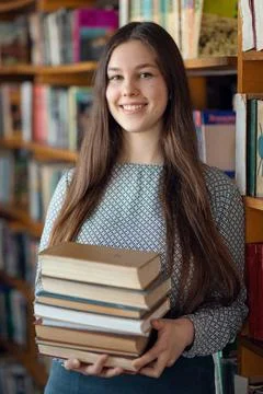 Portrait of a female student with a stack of books in library Stock Photos