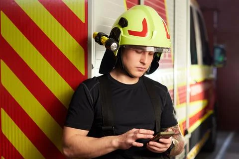 Portrait of a firefighter standing in front of a fire engine. Fireman using s Stock Photos