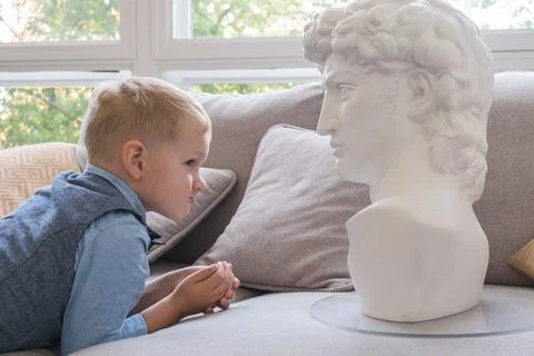 Portrait of a five-year-old boy in profile. Boy touches a plaster bust while  Stock Photos