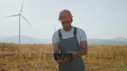 Portrait of focused indian man standing on field with wind turbines and using Stock Footage 170591177
