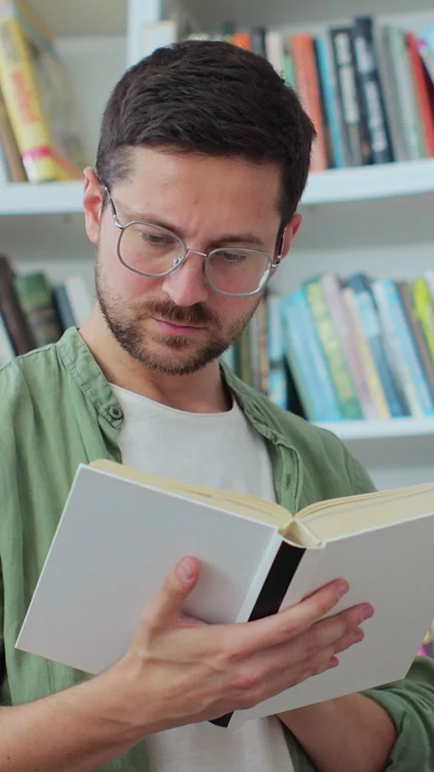 Portrait of focused man in glasses reading book from bookshelf for his class Stock Footage 345146131