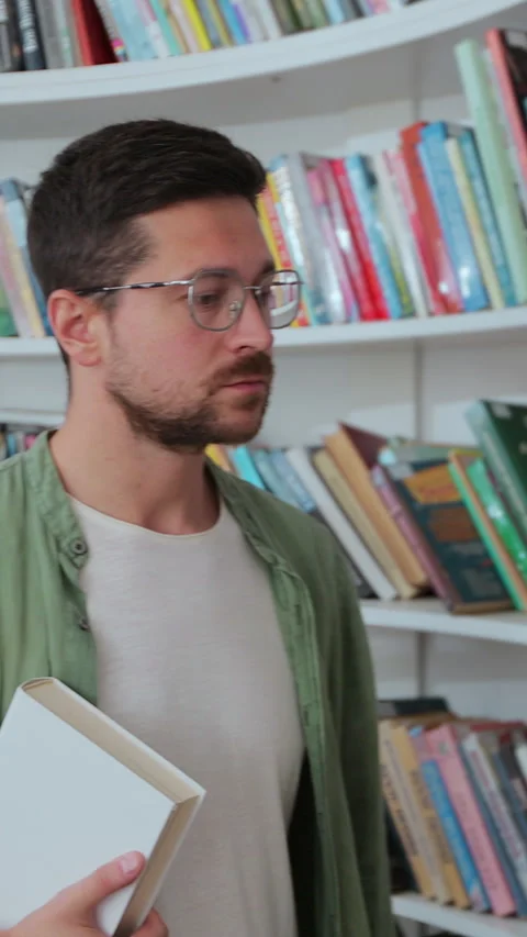 Portrait of focused man in glasses reading book from bookshelf Stock Footage 345146755