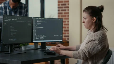 Portrait of focused programer writing code looking at multiple computer screens Stock Footage 168233313