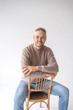 Portrait of a friendly, middle-aged man sitting on a simple wooden chair agai Stock Photos