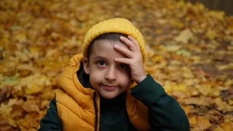 Portrait of a funny boy child without 2 teeth sitting in autumn in maple leaves Video stock 219222496