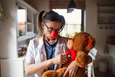 Portrait of funny female doctor with red clown nose holding teddy bear. Stock Photos