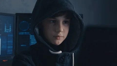 Portrait of a Genius Boy Hacker Prodigy in the hood working on computer in Vidéo 101980233