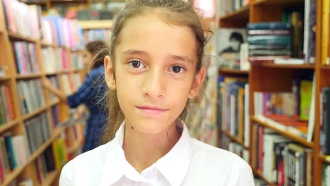Portrait of a girl 8 - 12 years old, standing in the library. Bookshelves of a Stock Footage