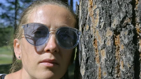 Portrait of a girl looking at the camera leaning against a tree trunk Stock Footage 149674953