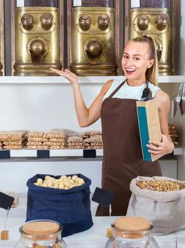 Portrait of girl seller who is standing near showcase with nuts in alimentacion Stock Photos