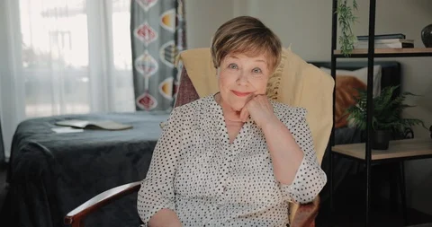 Portrait of good looking elderly lady sitting on chair and propping head at home Stock Footage 127180221