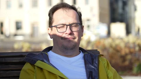 Portrait of good looking guy in glasses sitting on bench in city park, looking Stock Footage 168135665