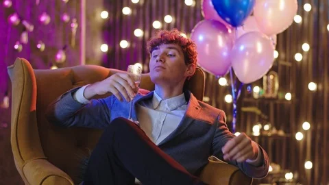 Portrait of a good looking guy on the sofa he have a stuff party holding a glass Stock Footage 122040882
