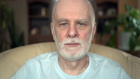 Portrait of good-looking handsome grim senior man sitting on chair at home Video stock 74639634