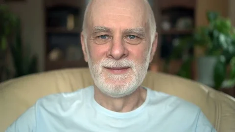 Portrait of good-looking handsome smiling senior man sitting on chair at home Stock Footage 74639357