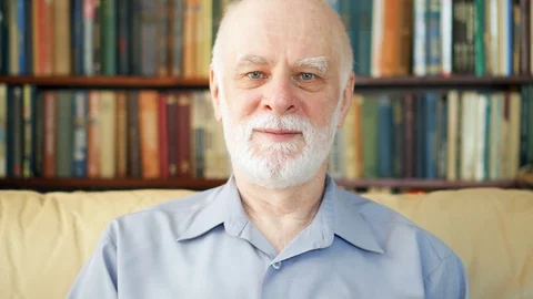 Portrait of good-looking handsome smiling senior man at home. Bookcase Stock Footage 85852810