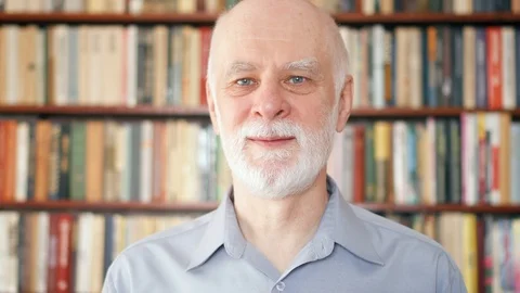 Portrait of good-looking handsome smiling senior man at home. Bookcase Stock Footage 87847192