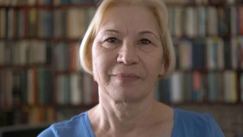 Portrait of good-looking happy smiling senior woman at home. Bookcase Stock Footage 74756364