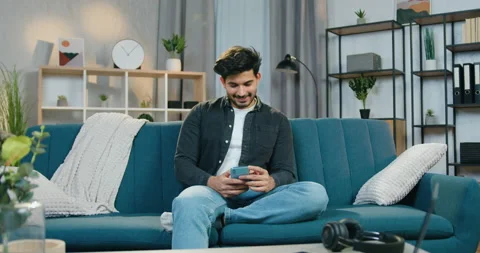 Portrait of good-looking happy smiling young bearded guy sitting on the couch at Stock Footage 150156485