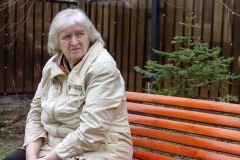 Portrait of the grey haired sad elderly woman sitting on the the park bench Stock Photos
