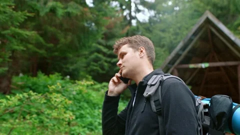 A portrait of a guy with a backpack stands in the forest and talks on the phone. Stock Footage 197874376
