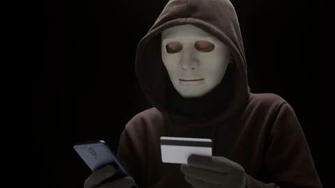 Portrait of hacker in anonymous mask using phone and credit card in dark room.  Stock Footage 290432645