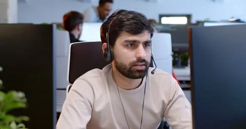Portrait of handsome Arab man in headset sitting at computer screen and talking Stock Footage 179985997