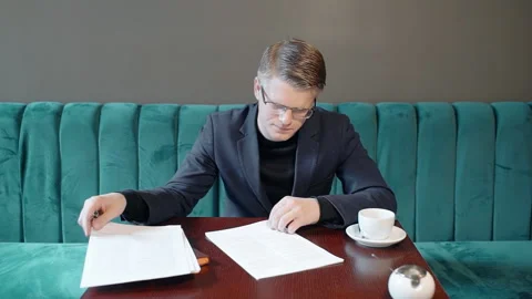 Portrait of handsome businessman reading documents and drinking coffee in cafe. Video stock 89953122