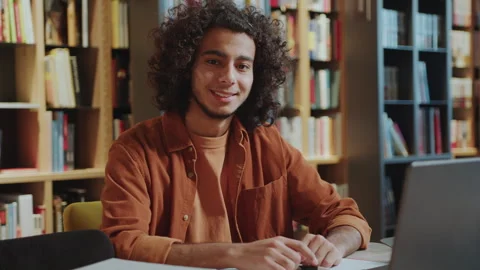 Portrait of Handsome Curly-Haired Guy at Desk in University Library Stock Footage 277699735