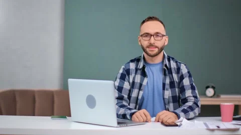 Portrait of handsome guy in glasses posing at table in front of laptop. Medium Video stock 143873372