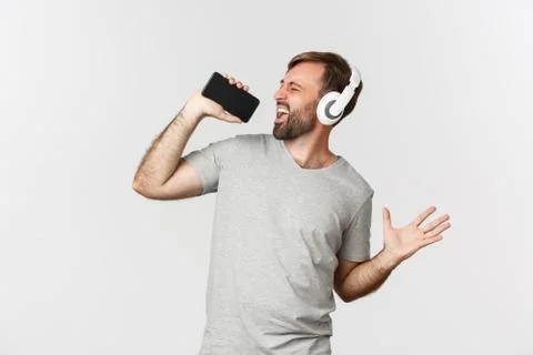 Portrait of handsome guy in gray t-shirt, playing karaoke app in headphones Stock Photos