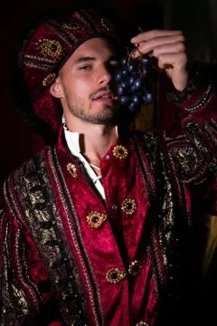 Portrait of handsome king with beard dressed in costume eating grapes and Stock Photos