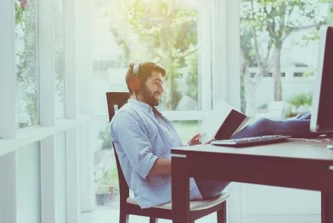 Portrait of handsome man with beard reading book and listening to music onlin Stock Photos