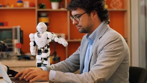 Portrait of handsome man in glasses making a program for robot on his laptop in Stock Footage 82497685