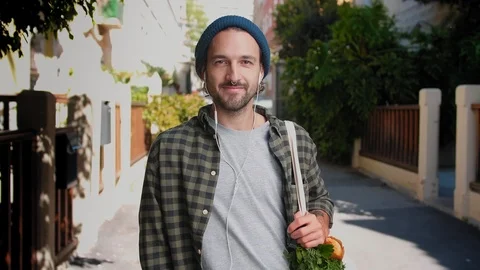 Portrait of handsome man with piercing using earphones and holding Eco shopper Stock Footage 111071330