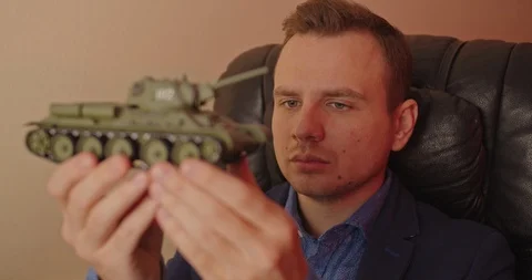 Portrait of handsome man with small model prototype  of tank.He carefully spinin Stock Footage 118823888