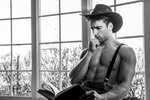 Portrait of handsome shirtless cowboy wearing hat sitting in window with book in Stock Photos