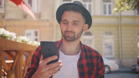 Portrait handsome young man in the hat uses phone walk in city smile feel happy Stock Footage
