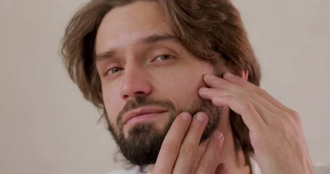 Portrait of handsome young man looking at camera, touching face and looks Stock Footage 142528639