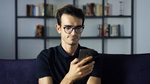 Portrait of Handsome Young Man texting by Phone Relaxing on the Sofa, Digital Stock Footage 93256387