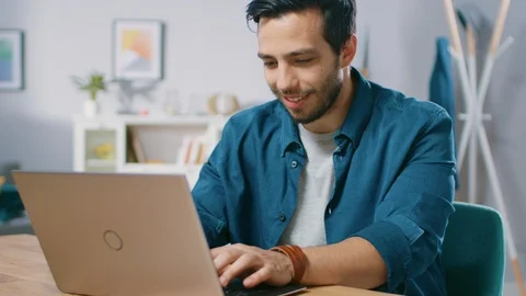 Portrait of Handsome Young Man Using Laptop Computer at Home, Watching and Laugh Video stock 97520181