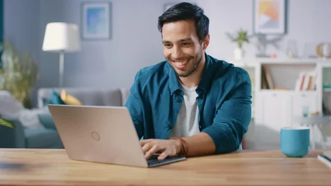 Portrait of Handsome Young Man Using Laptop Computer at Home, Watching and Laugh Video stock 97524873