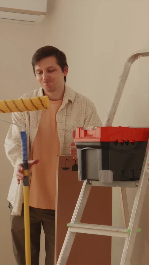 Portrait of handyman holding paint roller beside toolbox Stock Footage 346396463