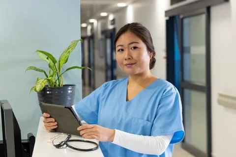Portrait of happy asian female doctor with tablet standing at hospital rece.. Stock Photos