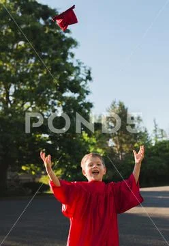 Portrait of happy boy in graduation gown throwing mortarboard on footpath Stock Photos